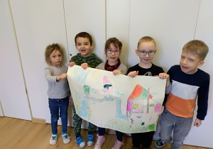 Pięcioro dzieci stoi w szeregu. Za nimi jest biała szafa. Dzieci trzymają przed sobą duży karton. Na kartonie narysowana jest przez dzieci oczyszczalnia ścieków.